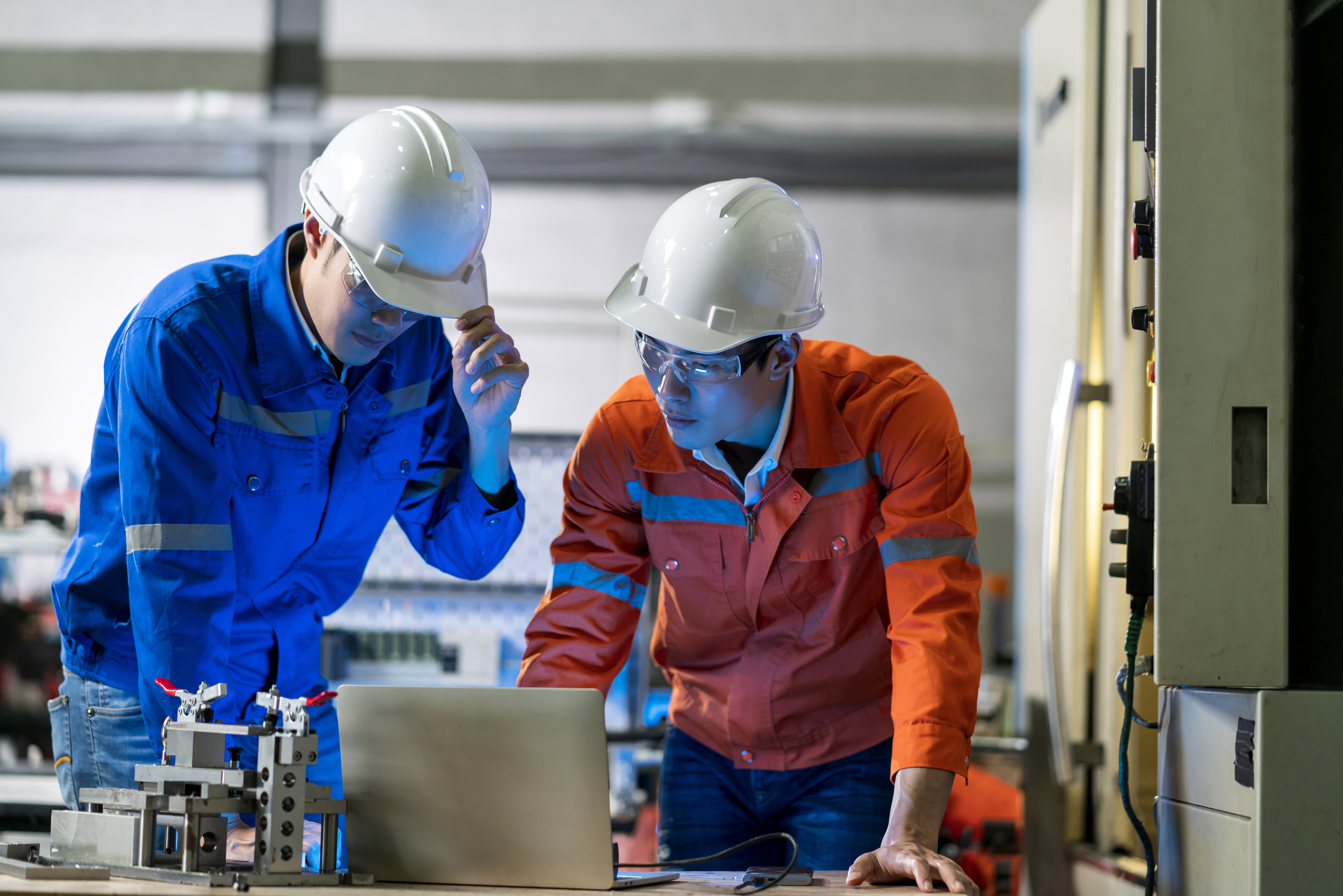 Male Asian engineer professional  having a discussion standing concult cnc machine in the factory ,two asian coworker brainstorm  explaining and solves the process of the cnc operate machine